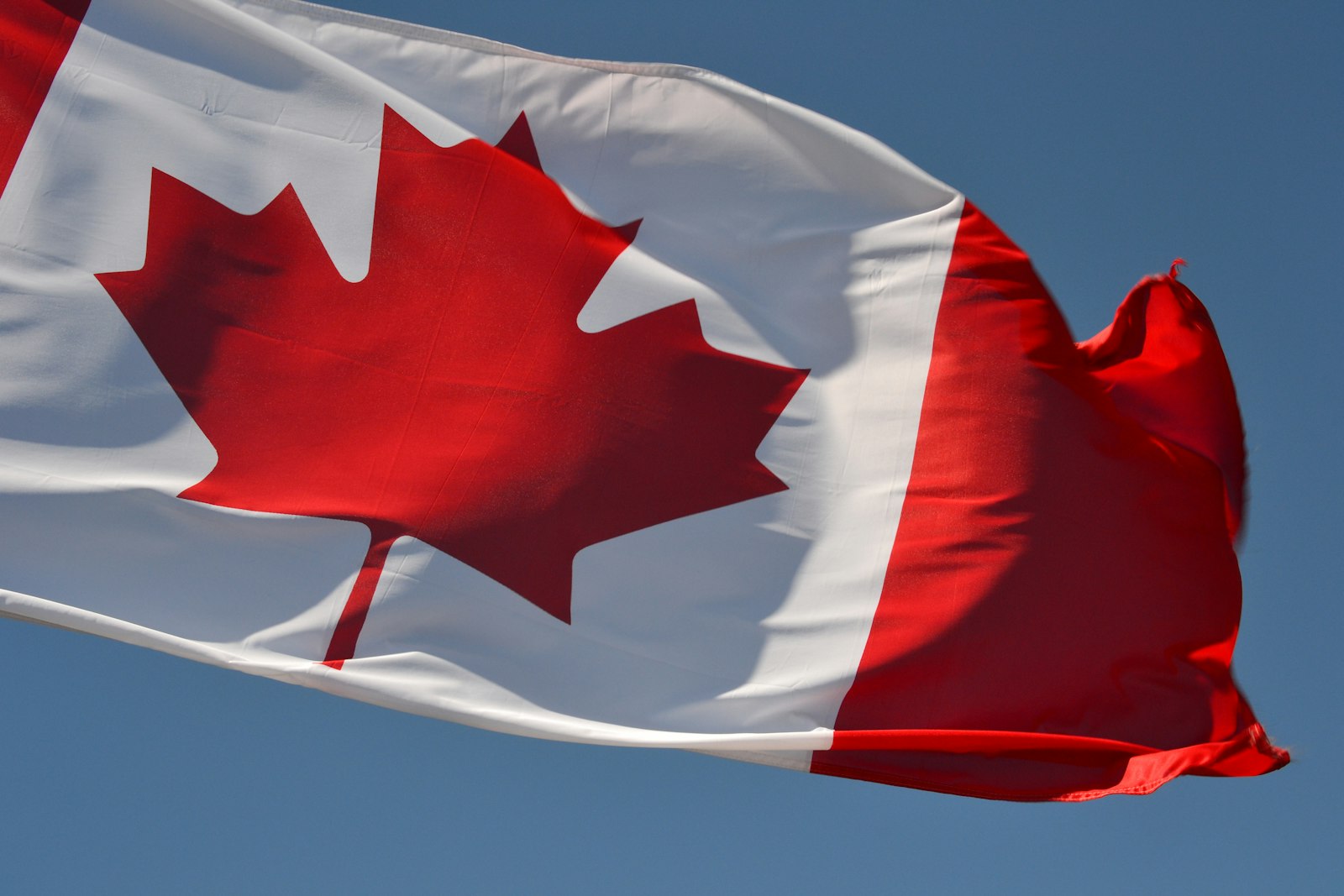 A Canadian flag with a red maple leaf against a blue sky
